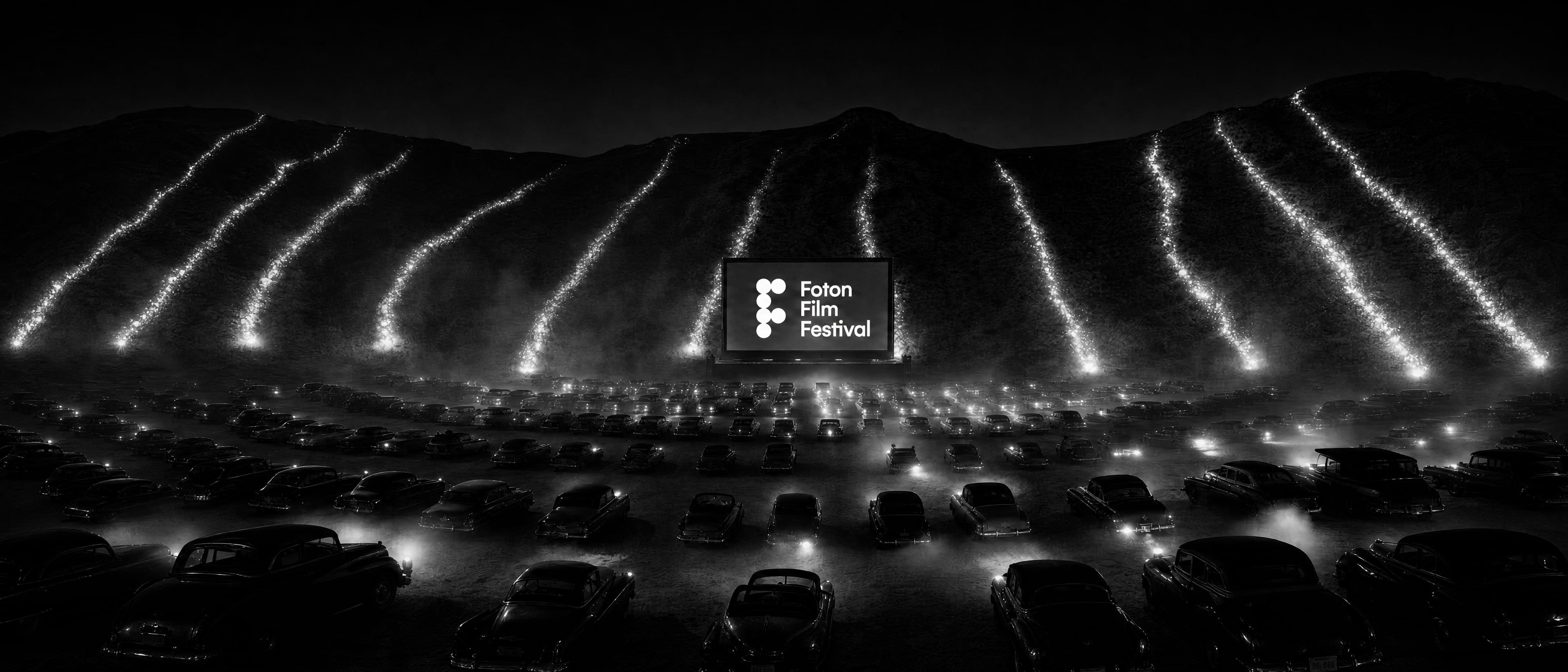The FOTON FILM FESTIVAL stage at night: rivers of light descending the hillside toward the screen, above a sea of parked cars.